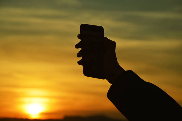 Male hand holding smart phone at the sunset - Photo, Image
