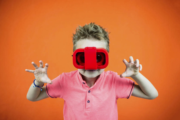 grappige jongen speelt in glazen van virtual reality voor de telefoon op een helder oranje achtergrond - Foto, afbeelding