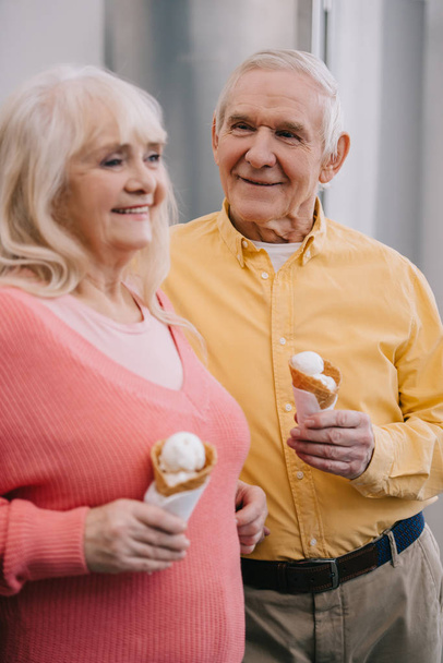smiling senior couple holding ice cream cones at home  - Foto, Imagen
