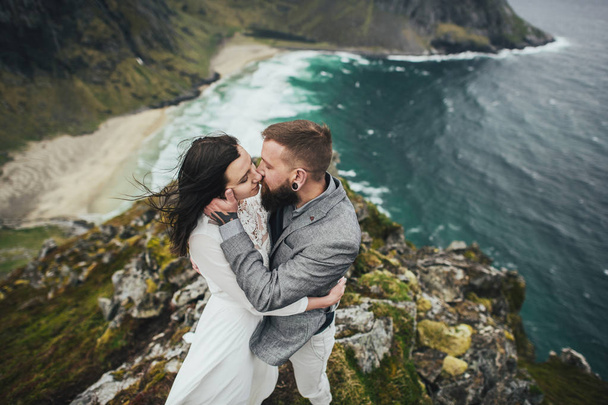 Happy wedding couple travelers kissing on hill at Kvalvika beach, Norway - Fotó, kép