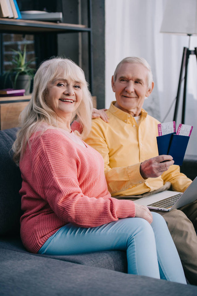 усміхнена старша пара сидить на дивані з авіаквитками та паспортами вдома
  - Фото, зображення