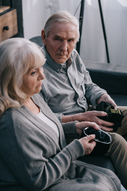 sad senior couple sitting on couch and holding wallets at home - Photo, Image