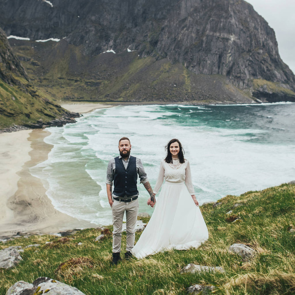 Happy wedding couple travelers walking on hill at Kvalvika beach, Norway - Фото, зображення