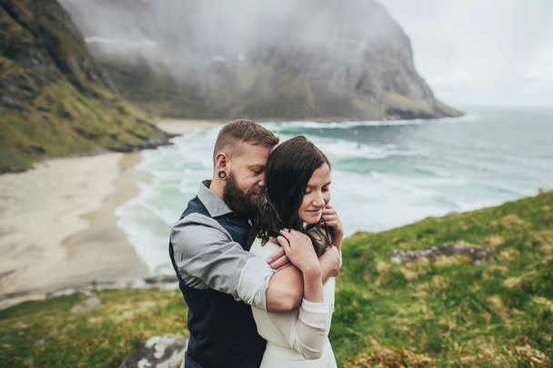 Happy wedding couple travelers hugging on hill at Kvalvika beach, Norway - Photo, image