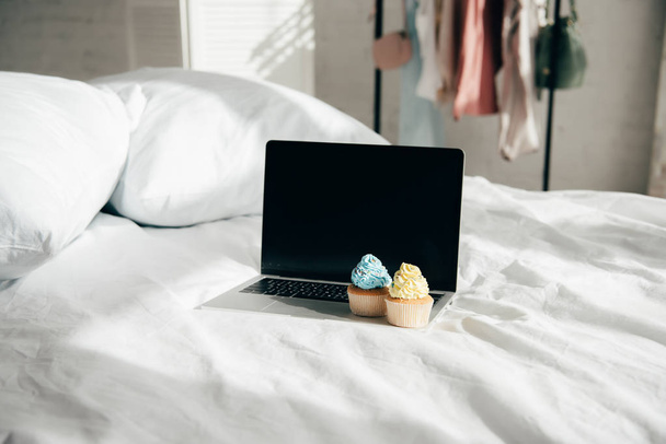 pastelitos dulces y sabrosos en el ordenador portátil con pantalla en blanco en el dormitorio
 - Foto, Imagen