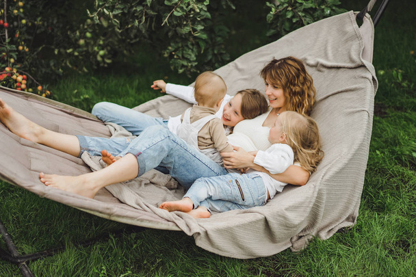 mother with children having fun in a hammock. Mom and kids in a hammock. The family spends time with the children in the garden. - Foto, imagen