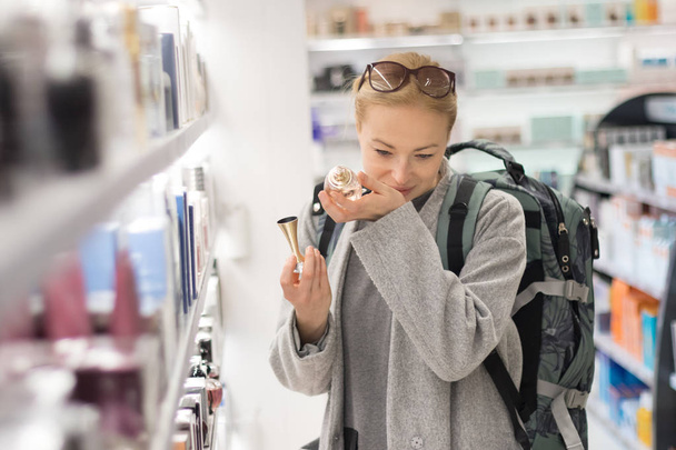 Szőke fiatal női utas fárasztó utazás hátizsák választott parfüm, a repülőtéri vámmentes bolt. - Fotó, kép