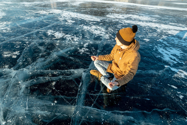 Podróżnik medytuje, siedząc w pozycji lotosu na czysty lód jezioro Bajkał. Podróż do pięknych miejsc o charakterze - Zdjęcie, obraz