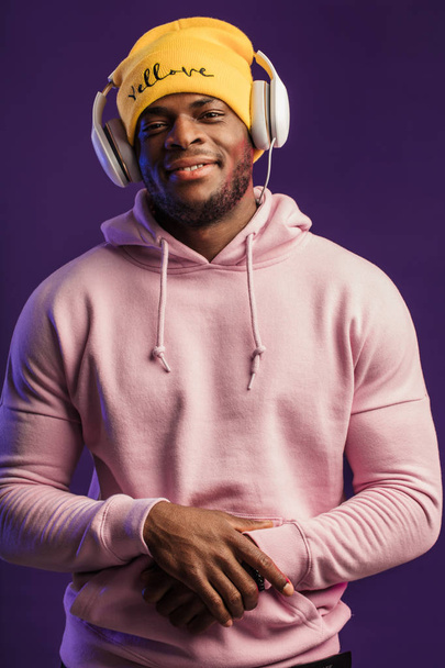 Afrikanischer Mann im Kapuzenpullover mit Kopfhörern, fröhlicher Gesichtsausdruck. Musik, Menschen - Foto, Bild