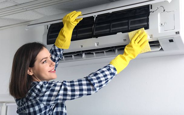 Jeune femme nettoyage climatiseur à la maison
 - Photo, image