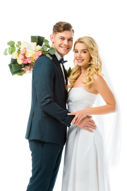 smiling bride with wedding bouquet hugging happy groom isolated on white - Zdjęcie, obraz
