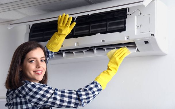 Jonge vrouw reinigen airconditioner thuis - Foto, afbeelding