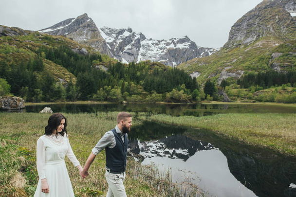 Happy wedding couple travelers walking on shore of lake, Lofoten, Norway  - Photo, image
