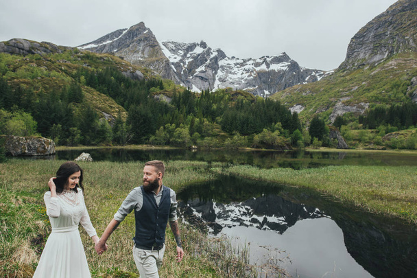 Happy wedding couple travelers walking on shore of lake, Lofoten, Norway  - Foto, imagen