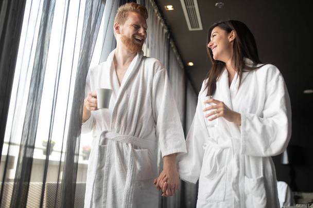 Happy young couple in white bathrobes drinking coffee together. Hotel, travel, relationships, and happiness concept - Fotó, kép