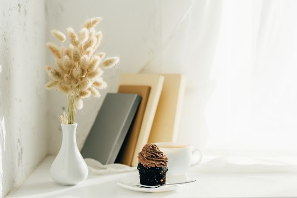 Weidenkätzchen in der Vase neben Cupcake, Kaffee und Büchern  - Foto, Bild