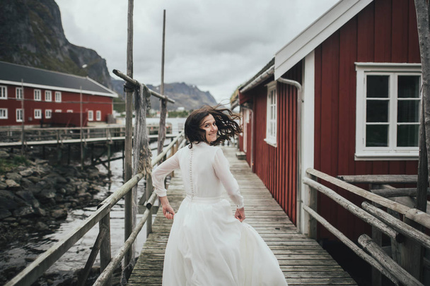 Portrait of happy bride in romantic wedding dress on red houses background, Lofoten, Norway - Photo, Image