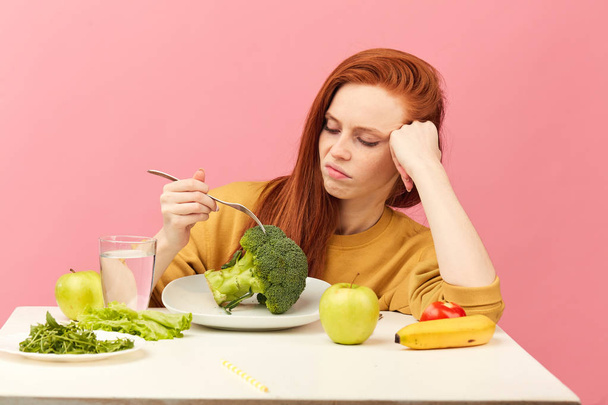 Vegetable diet. Sad dull woman holding broccoli on fork while making grimace - Фото, изображение