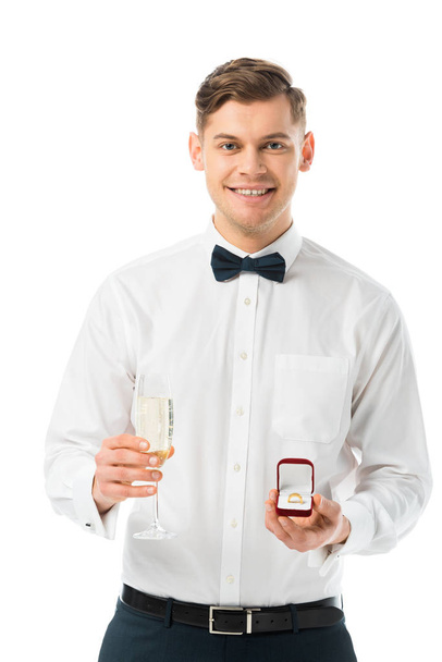 happy groom holding glass of champagne and gift box with wedding ring isolated on white - Photo, Image