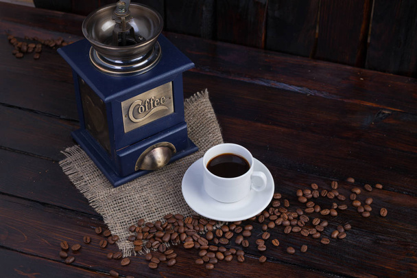 コーヒー グラインダーとリネン布で暗い背景の木に熟したコーヒー粒の横にコーヒーの白いカップ - 写真・画像