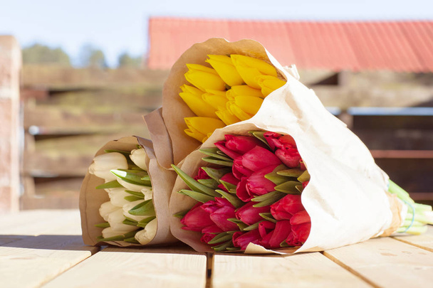 De beaux bouquets colorés de tulipes en papier artisanal reposent dans la rue sur une table en bois. Vue latérale
 - Photo, image