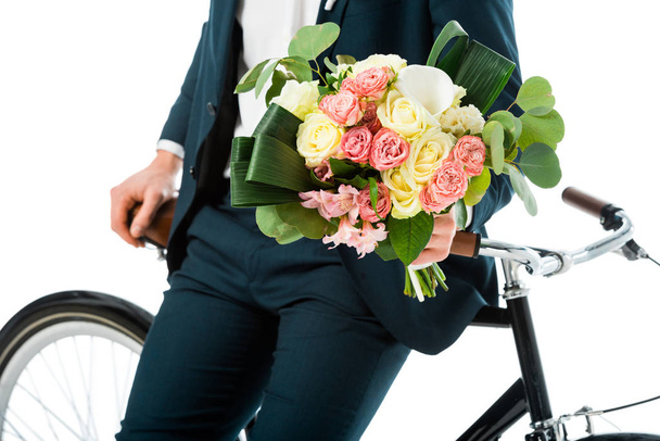 gedeeltelijke weergave van bruidegom permanent in de buurt van fiets ingedrukt te houden bruiloft boeket geïsoleerd op wit - Foto, afbeelding