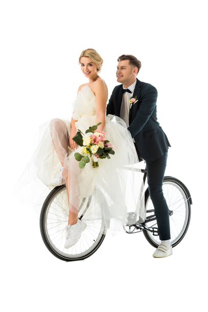 beautiful bride holding wedding bouquet while sitting on bicycle together with groom isolated on white - Photo, Image