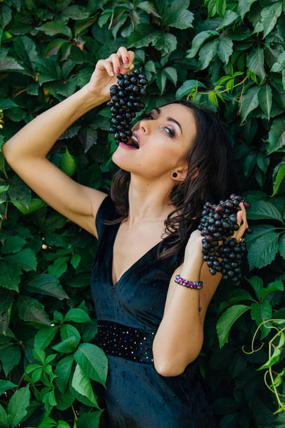 Portrait of young sexy brunette biting black grapes. - Valokuva, kuva