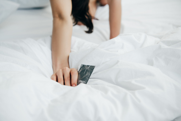 cropped view of woman holding condom on white bed - Photo, Image