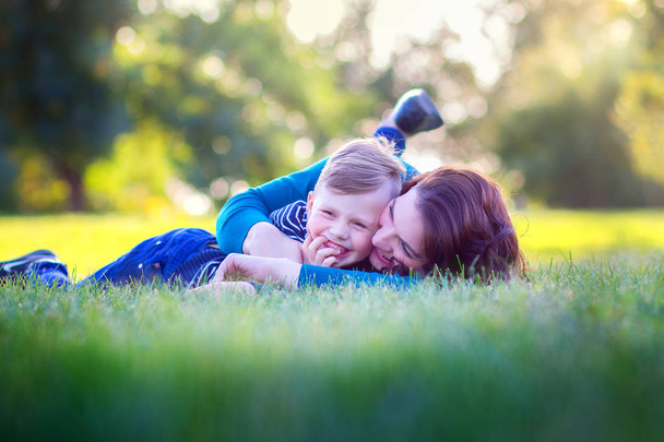 Young mother with the son lie on a grass in the park and joyfully embrace - Fotografie, Obrázek