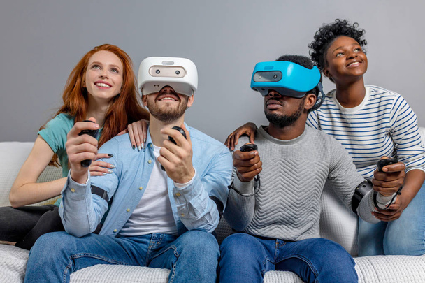 Two guys playing video games using VR glasses and girlfriends support them. - Foto, Bild