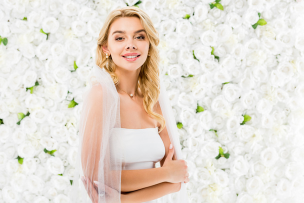 happy beautiful bride with blonde hair posing at camera on white floral background - Foto, imagen