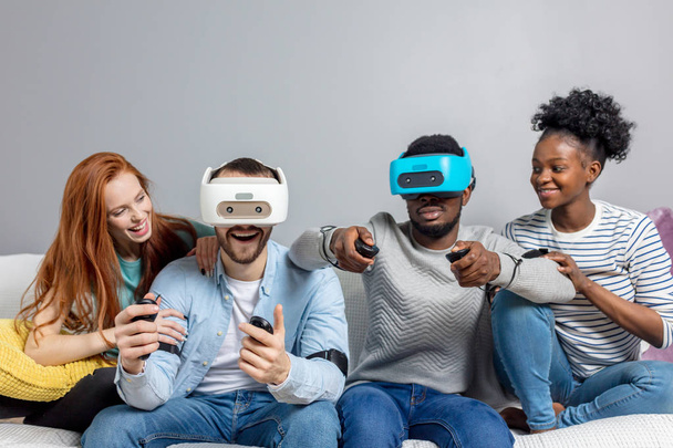 Two guys playing video games using VR glasses and girlfriends support them. - Фото, изображение