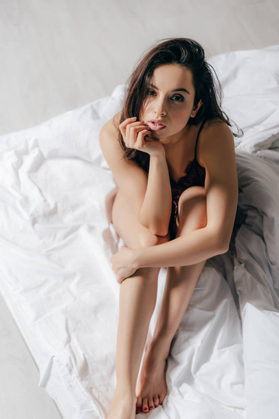 top view of sexy girl sitting on bed and looking at camera - Фото, изображение