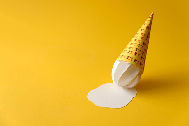 Melted paper vanilla ice-cream cone on yellow background. Copy space. Creative or art food concept - Photo, image