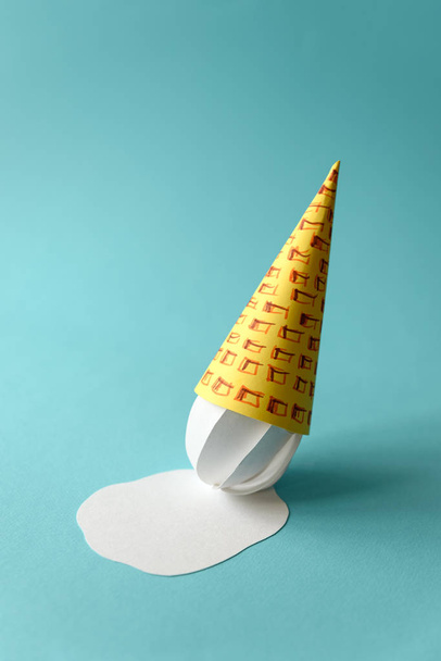 Melted paper vanilla ice-cream cone on blue background. Copy space. Creative or art food concept - Фото, зображення