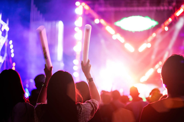 Duas mulheres amigas acendem luzes de palco de concerto e pessoas fãs silhueta levantando mãos brilho vara no festival de música vista traseira com holofotes efeito brilhante
 - Foto, Imagem