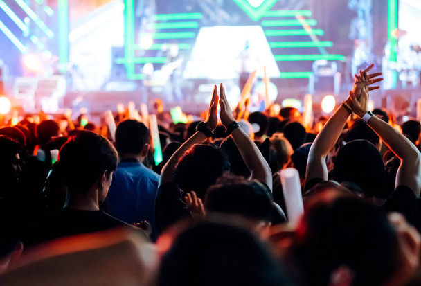 Tömeg tapsolni, vagy a koncert szakaszban fények és emberek rajongó közönség silhouette emelni kezét a zenei fesztivál hátsó nézet spotlámpa izzó hatás kezekkel - Fotó, kép