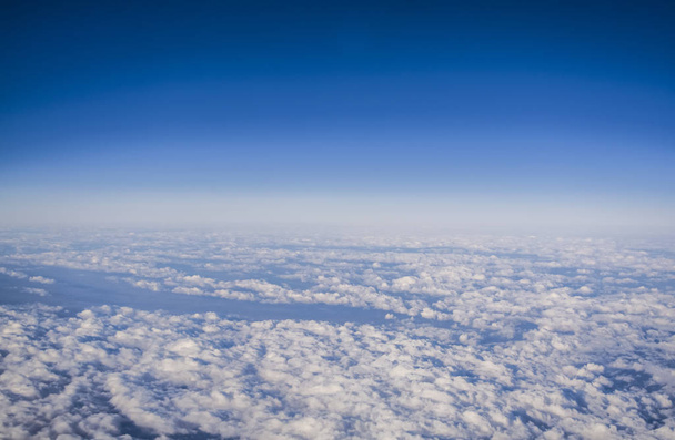 Uitzicht vanuit het raam van een vliegtuig op wolken en blauwe heldere hemel en de aarde vanuit de hoogte. Prachtig uitzicht vanuit de lucht van bergen.  - Foto, afbeelding