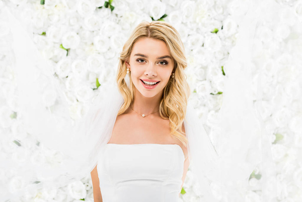 happy beautiful bride looking at camera on white floral background - Photo, Image