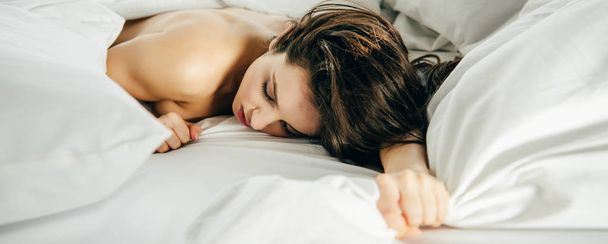panoramic shot of naked brunette girl lying on bed with closed eyes - Foto, Imagem