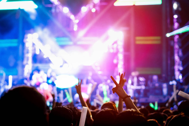 Hand gebaar overwinning vinger naar het concertpodium licht menigte of publiek artiest band in het muziek festival Achteraanzicht met schijnwerpers glowing effect en mensen fan publiek silhouet verhogen handen omhoog - Foto, afbeelding