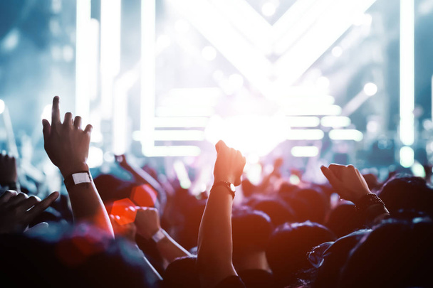 Multitud de manos arriba luces de escenario de concierto y la gente fan silueta audiencia levantando las manos en la vista trasera del festival de música con reflector efecto resplandeciente
 - Foto, Imagen