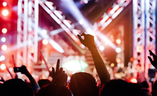 Menigte van handen omhoog concert podium verlichting en mensen fan publiek silhouet verhogen handen of gloed stok houden in het muziek festival Achteraanzicht met spotlight gloeiende ingang - Foto, afbeelding