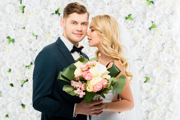 happy young bride and groom holding wedding bouquet on white floral background - Photo, Image