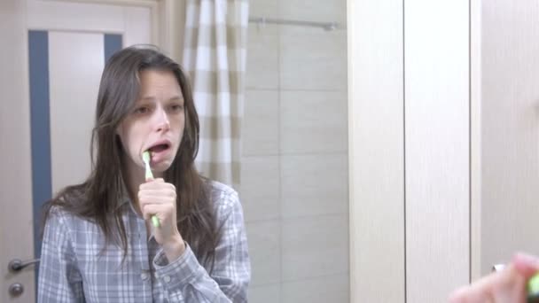 Sleepy woman brushing her teeth in the bathroom in front of the mirror. - Filmati, video