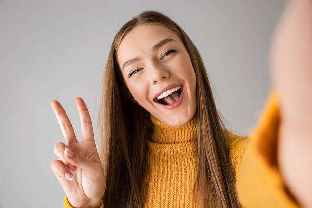 Happy young woman isolated over grey wall background take a selfie by camera. - Φωτογραφία, εικόνα