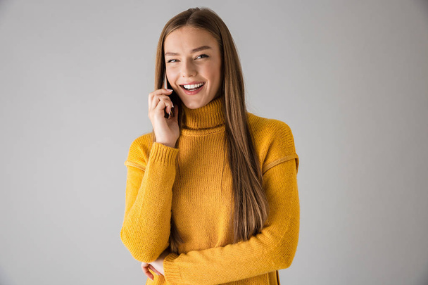 Happy young woman isolated over grey wall background talking by mobile phone. - Valokuva, kuva