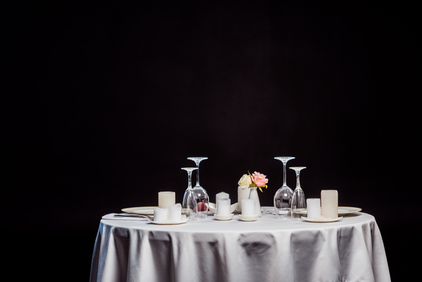 tabel met wit tafellaken, tafelgerei en kaarsen geïsoleerd op zwart - Foto, afbeelding