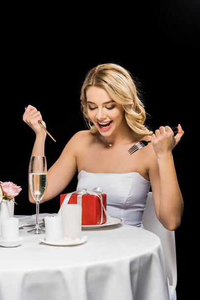 novia alegre con tenedor y cuchillo imitando comer con caja de regalo aislado en negro
 - Foto, imagen